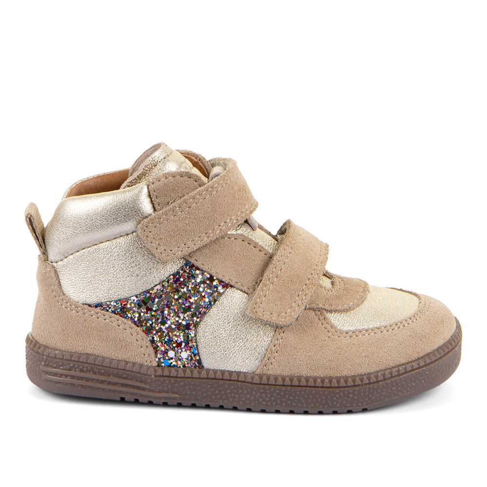 A toddler's high-top sneaker in beige suede and metallic silver leather, featuring a glittery multicolor star-shaped side panel and two hook-and-loop straps, shown against a light gold background.